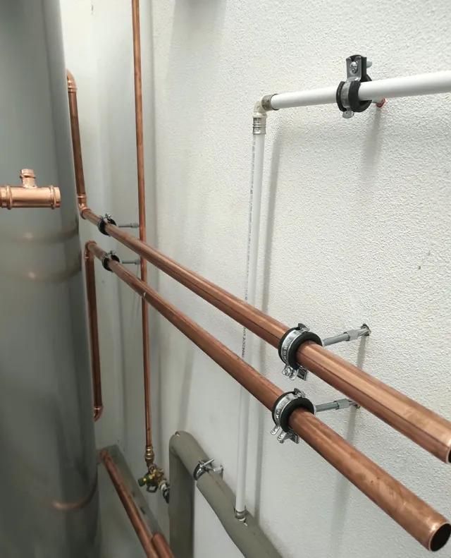 Parallel geführte Kupferleitungen mit Rohrschellen an der Wand des Technikraums