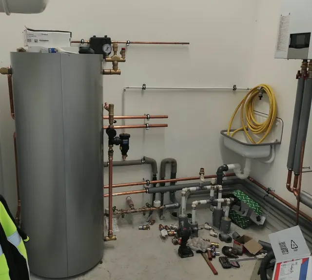 Pufferspeicher mit Pumpengruppe und Manometer, daneben die Heizkreisverteilung für zwei Haushälften während der Montage