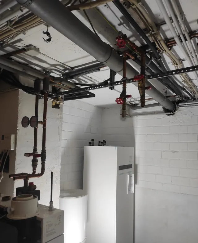 Aufgeräumter Technikraum mit Wärmepumpen-Innengerät, Speicher und Deckenverrohrung